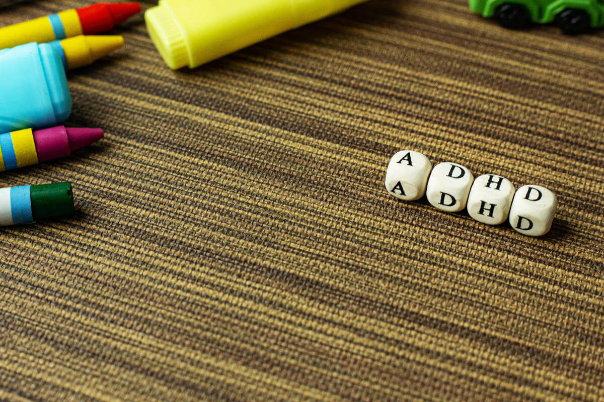 Dice spelling 'ADHD' next to crayons on a table mat
