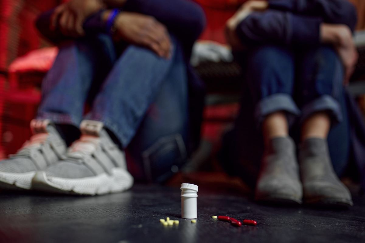 A pill bottle and loose capsules on the floor in front of two people seated on a couch