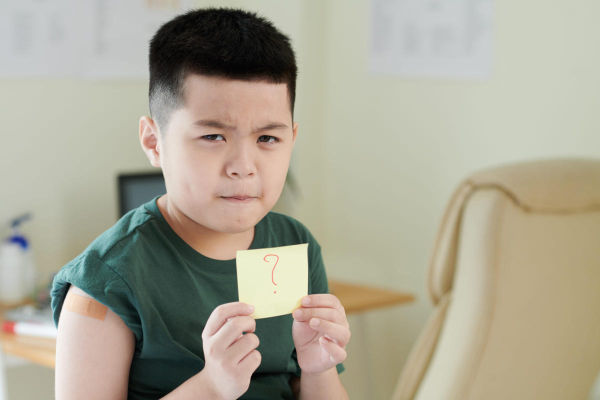Frowning little boy showing sticker note with question mark