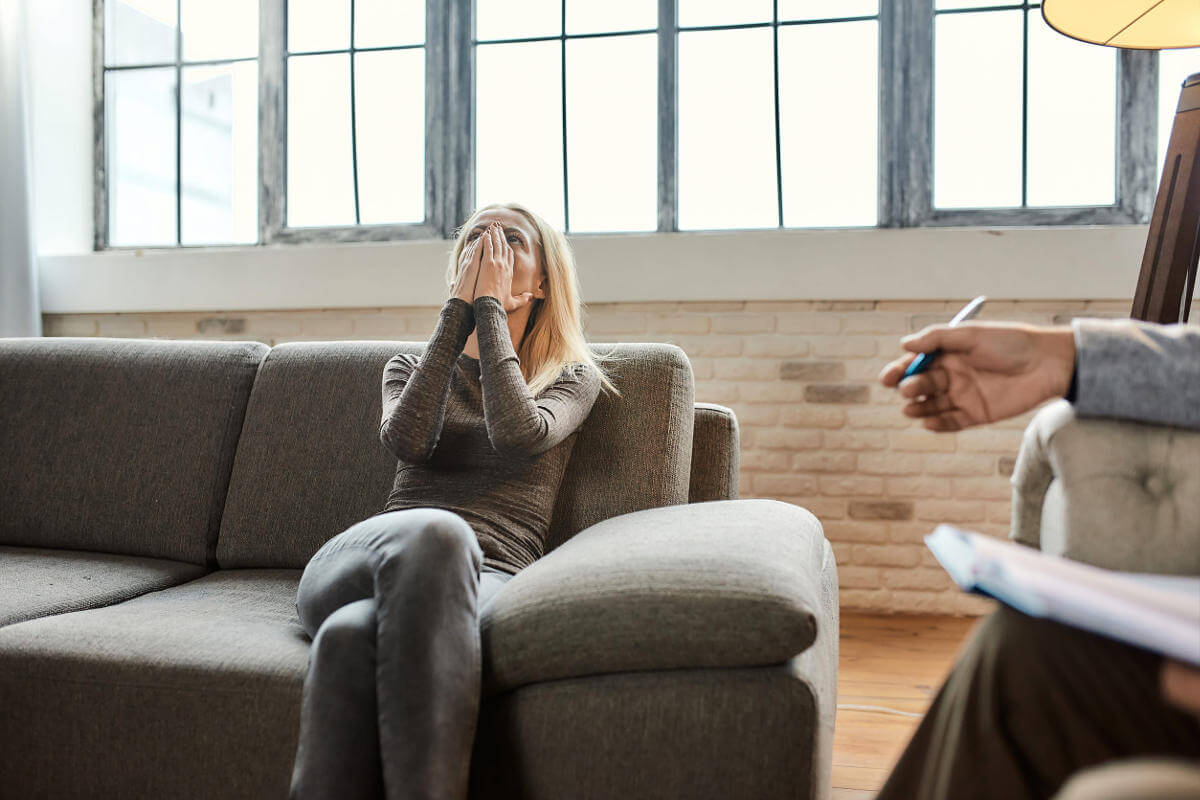 Depressed woman covering face, sitting on couch during therapy session