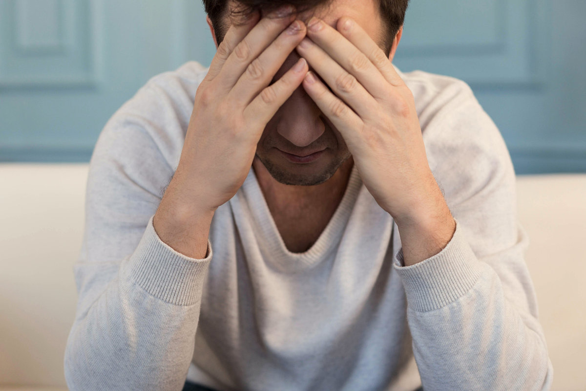 Sitting man covering face with hands