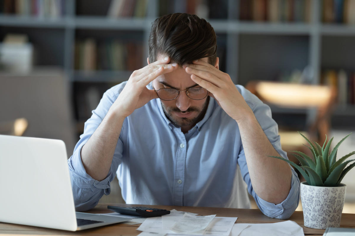 Frustrated young man in glasses sitting at table feeling stressed 