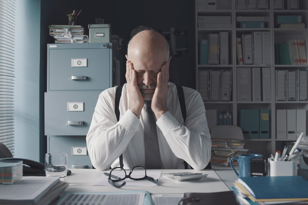 Exhausted corporate businessman sitting at desk with head in hands