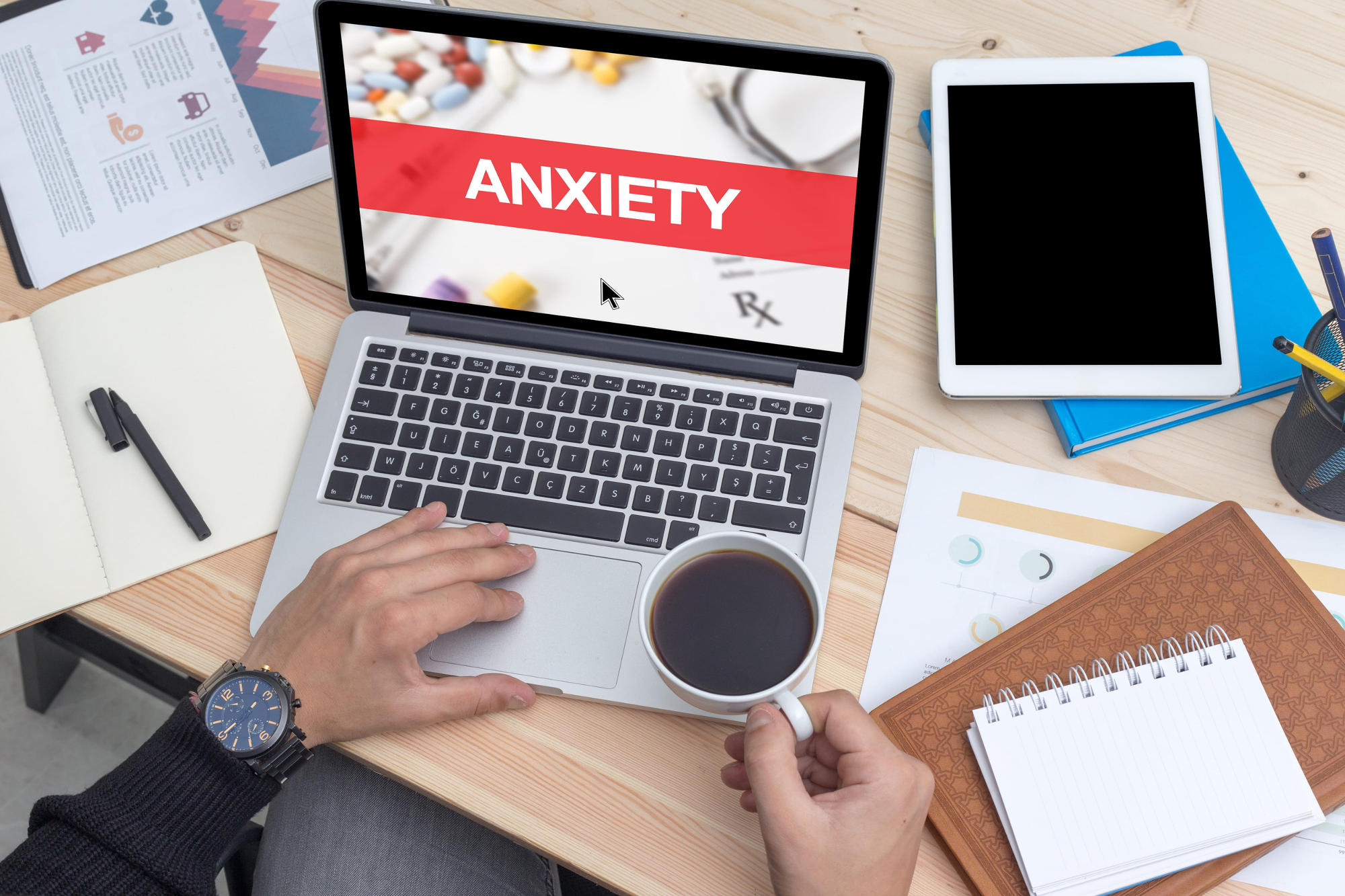 Man's hands holding coffee cup and using laptop that says 'ANXIETY' in white letters against red