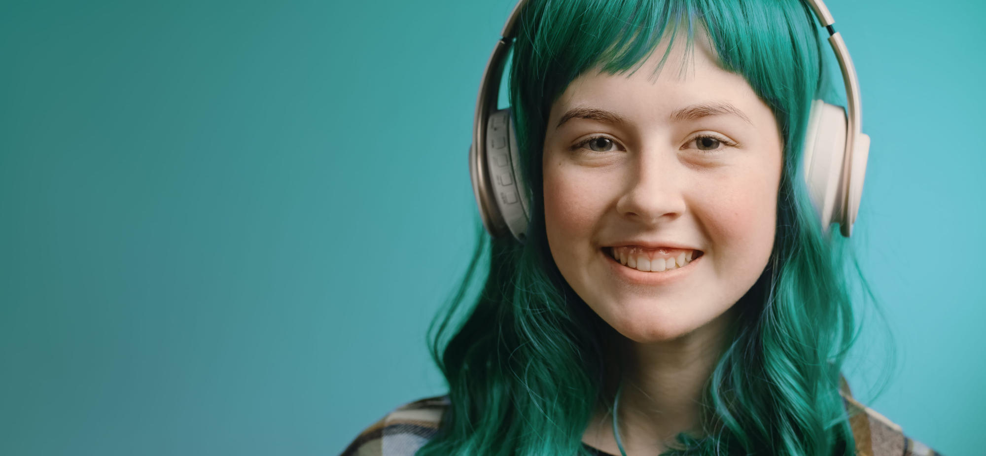 Gen Z teenager with green hair listening to music in headphones.