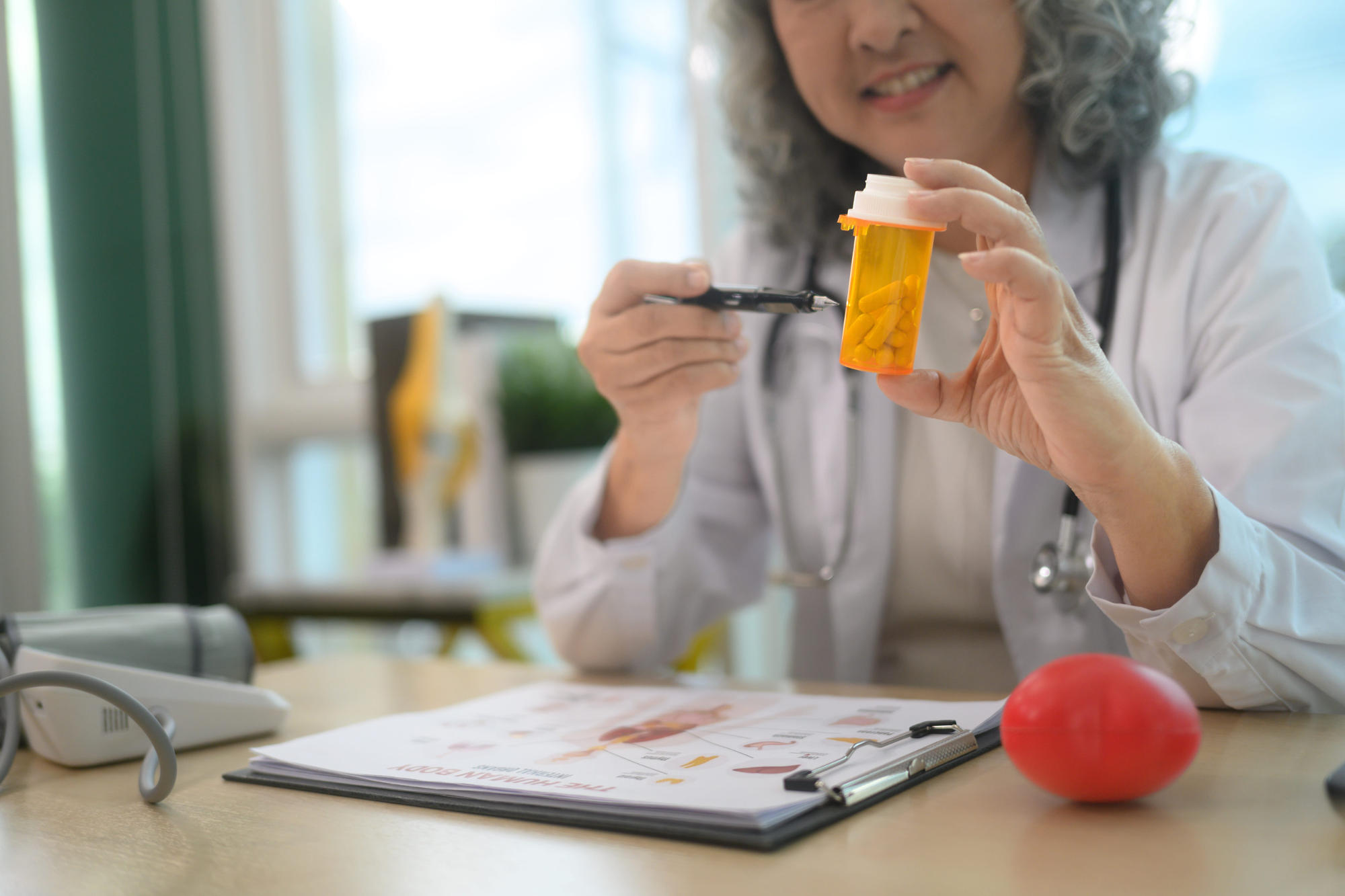 Medical professional holding medication container and pointing at it with a pen.