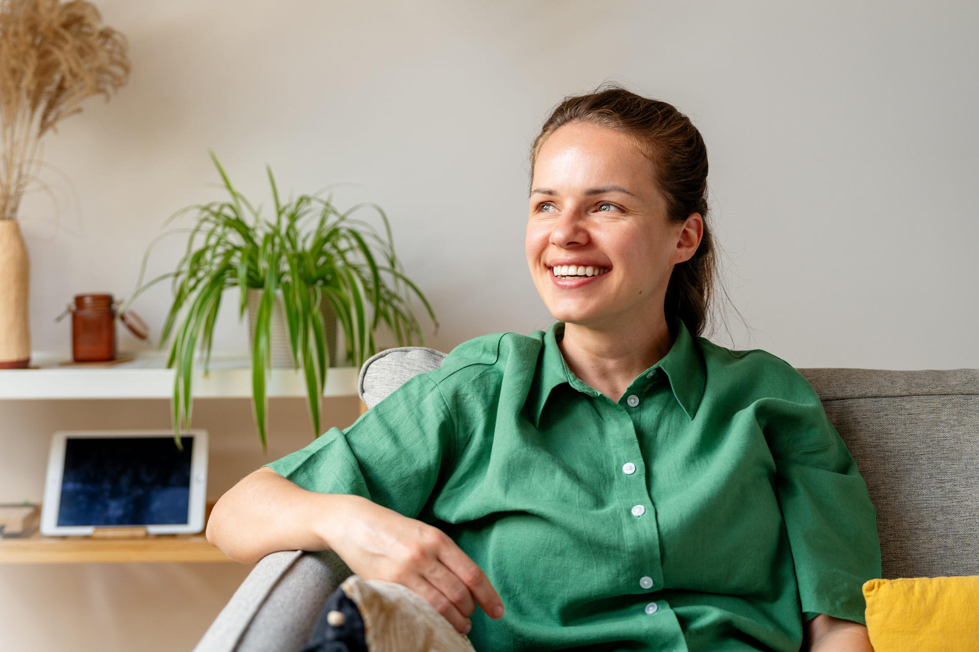 Young adult woman in green shirt sitting on sofa at home and smiling