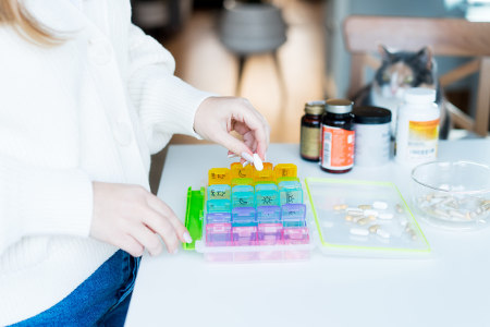 Woman's hands sorting pills into weekly medical pill organizer