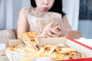 An image of a woman vomiting due to indigestion from overeating pizza, caused by binge eating disorder.