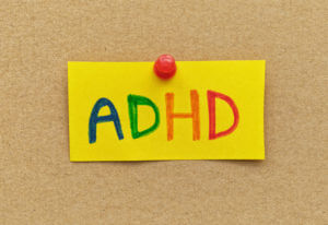 A yellow paper note with the abbreviation ADHD on it pinned to cardboard.
